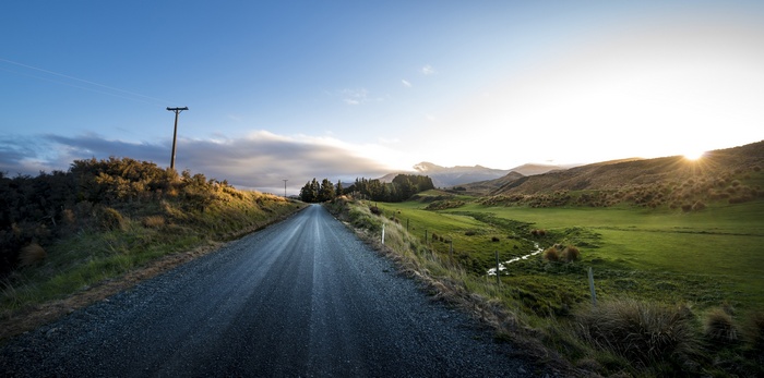 Gravel road through a green landscape at sunset