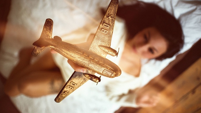 Woman holding a golden airplane model in bed