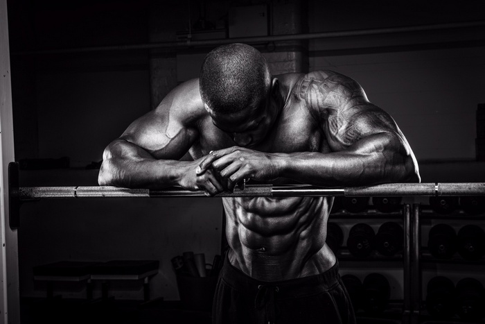 Black and white photo of a muscular man resting on a barbell