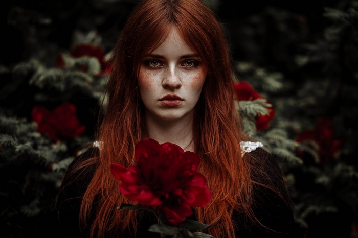 Redhead woman with freckles holding a red flower