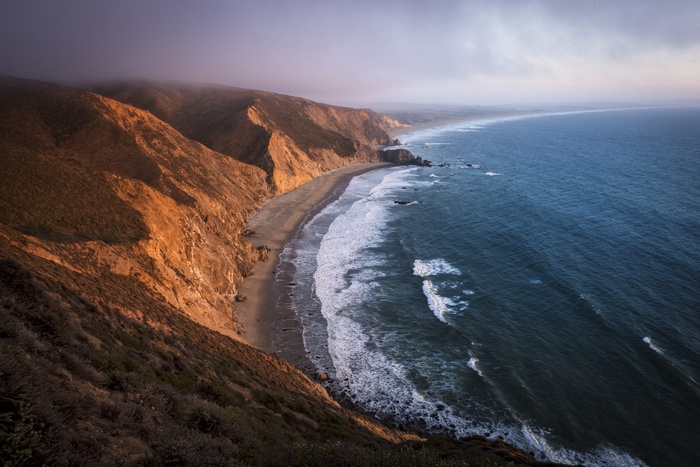 Coastal mountains meet the sea with waves and clouds