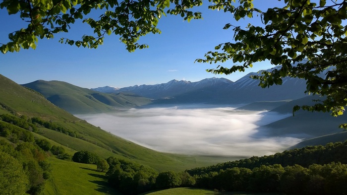 Misty valley with green mountains and snowy peaks in Italy