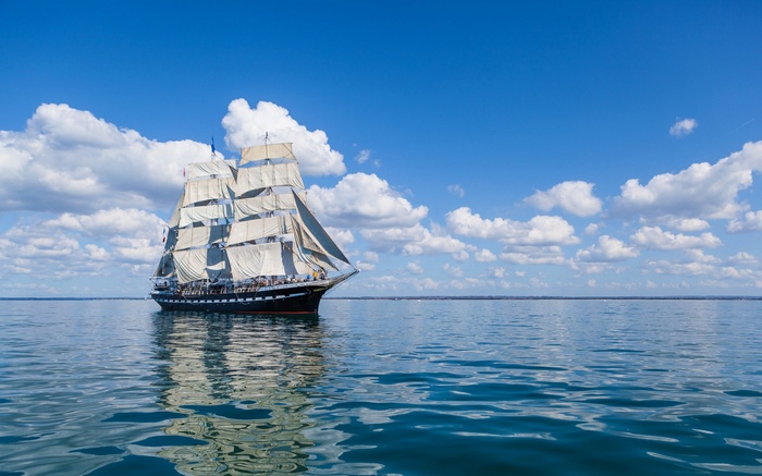 Tall ship sailing on a blue sea under clouds