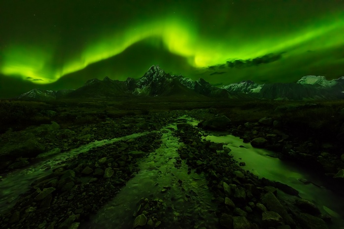 Aurora Borealis over snowy mountains and a rocky creek