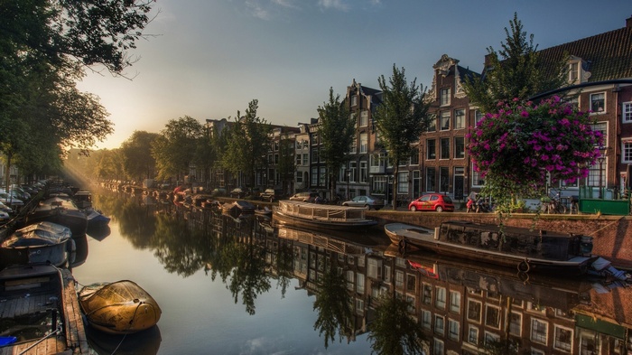 Amsterdam canal with houseboats and reflections at sunrise