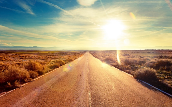 A long, empty road stretches towards the horizon under a bright sun.