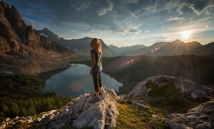 Woman standing on a rock overlooking a mountain lake at sunset