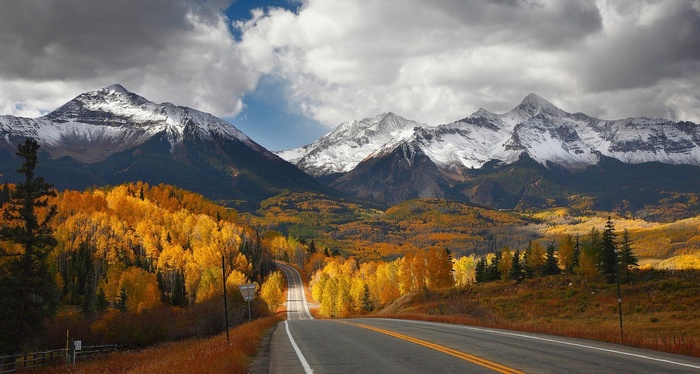 Road through autumn forest to snow-capped mountains