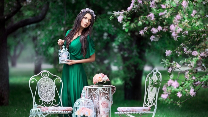 Woman in green dress holding a birdcage in a park