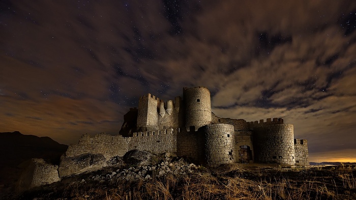 Ancient stone castle under a starry night sky with clouds