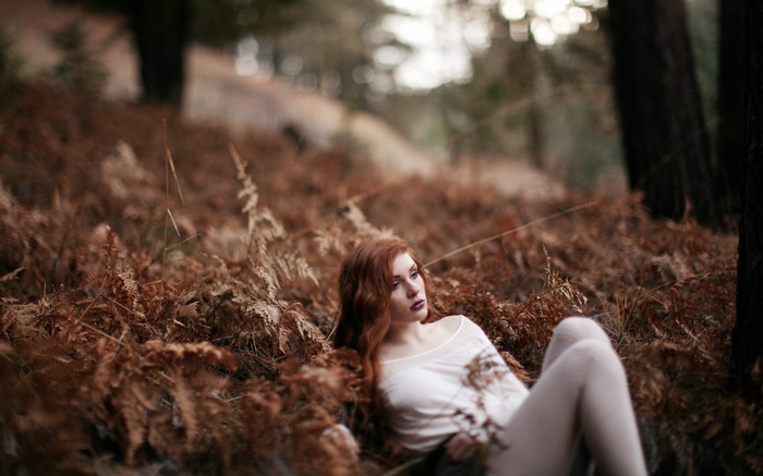 Redhead woman lying in dry ferns in a forest