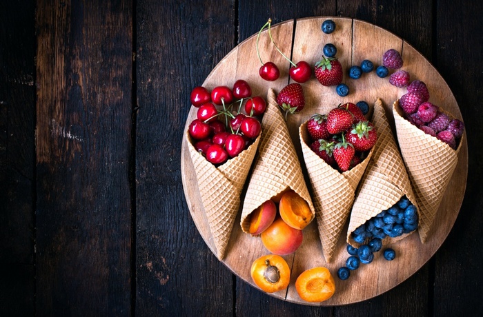 Waffle cones filled with fresh berries and apricots on a wooden board
