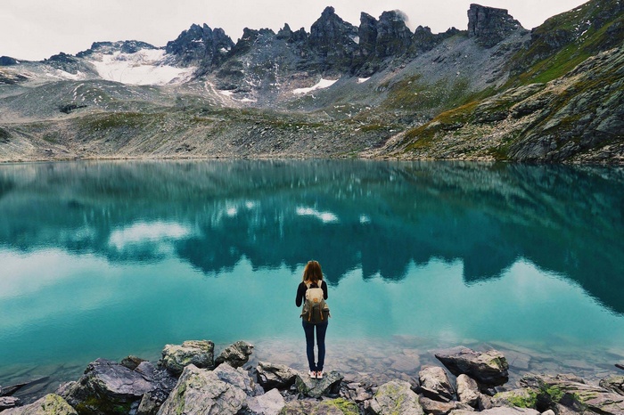 Woman with backpack by turquoise lake and mountains