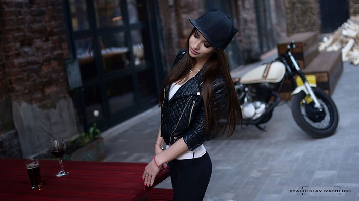 Woman in leather jacket and baseball cap with motorcycle