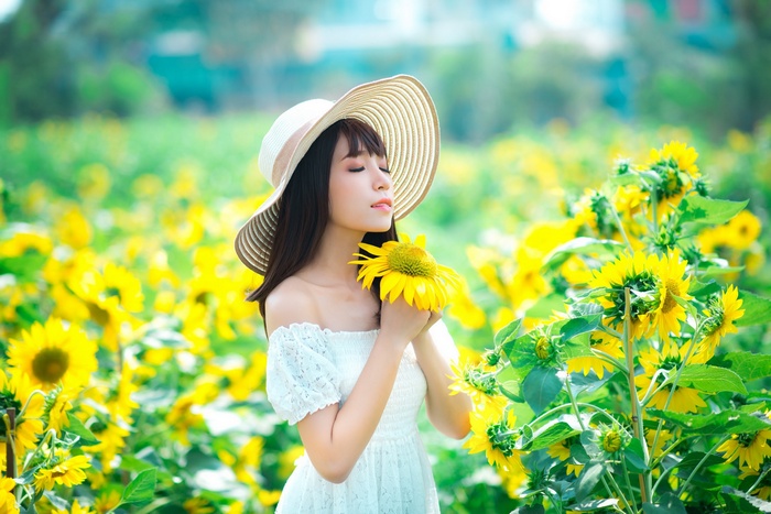 Woman in a hat holding a sunflower in a field