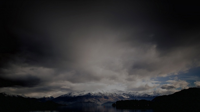 Snow-capped mountains over a dark lake under stormy clouds