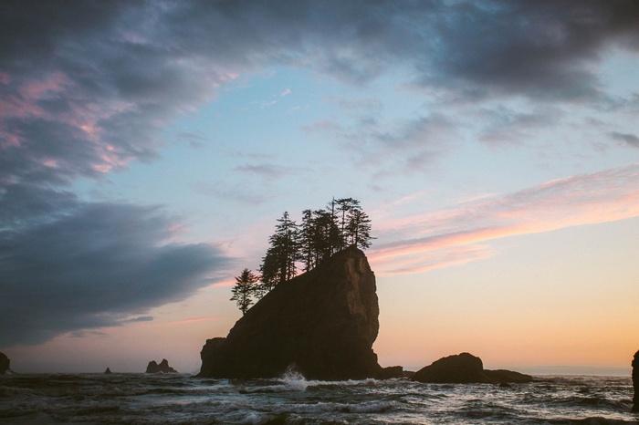 Rocky island with trees in the ocean at sunset