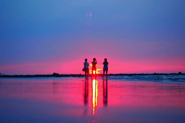 Three people silhouetted against a vibrant sunset on a beach