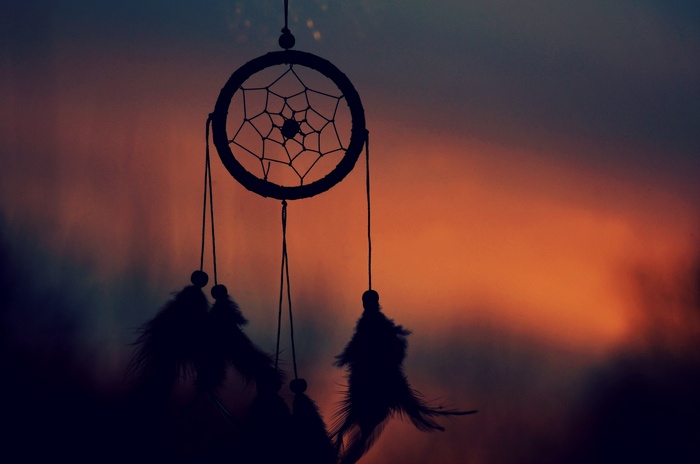 Silhouette of a dreamcatcher against a sunset sky
