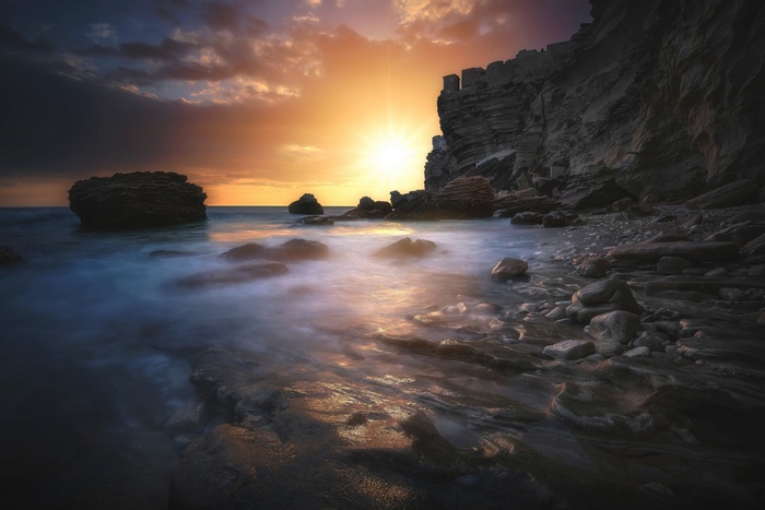 Sunset over rocky coastline with crashing waves