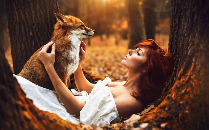 Woman with red hair and fox in autumn forest