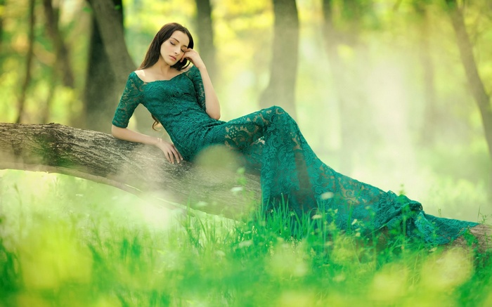 Woman in a green lace dress sitting on a log