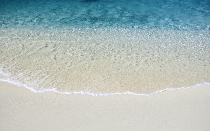 Clear blue sea waves washing onto a white sand beach