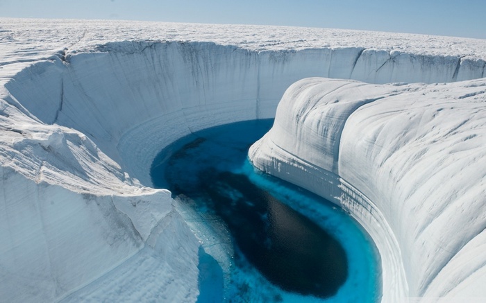 A deep blue meltwater stream carves through a Greenland glacier