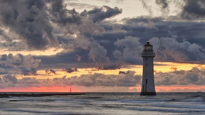 Lighthouse on the sea at sunset with dramatic clouds