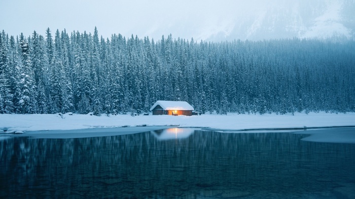 Snowy cabin by a frozen lake with pine trees