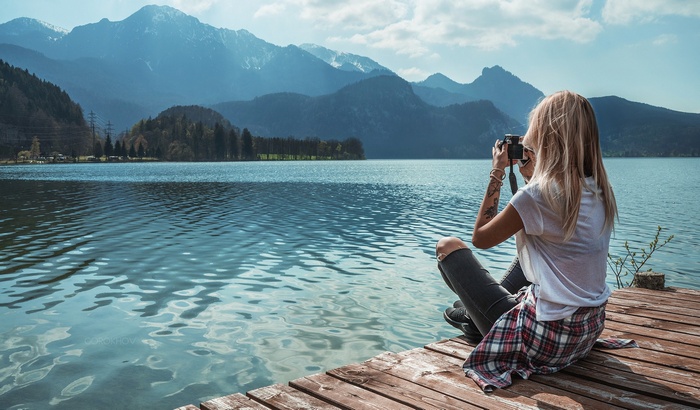Woman with camera on pier by lake and mountains
