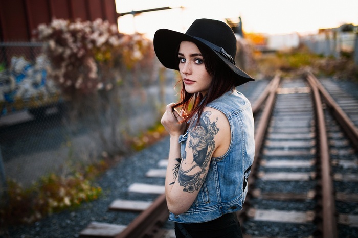 Woman with tattoos wearing a hat on train tracks