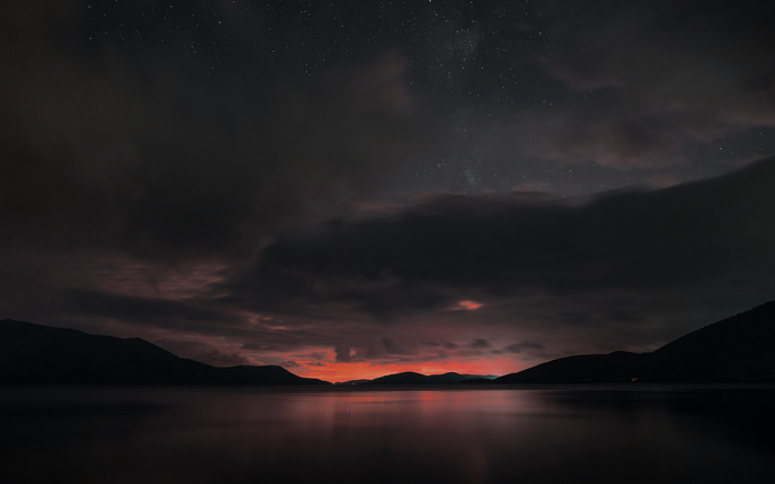 Dark lake and mountains under a starry, cloudy sky