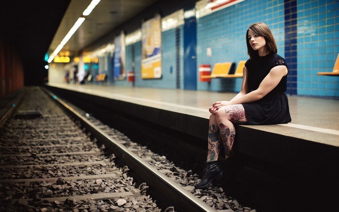 Woman with tattoos sitting on a train platform