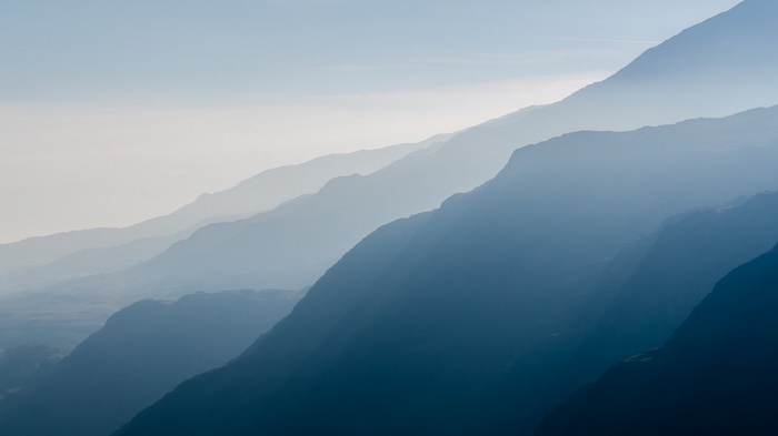 Layered mountains shrouded in mist under a pale sky