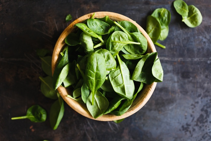 Bowl of fresh spinach leaves on a dark surface