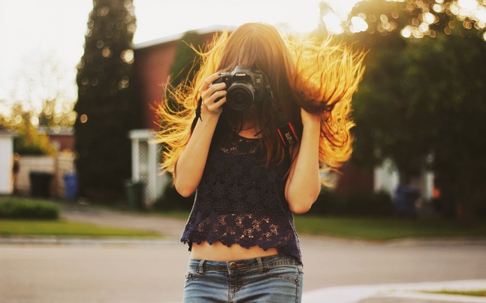 Woman holding a Canon camera with hair blowing in sunlight