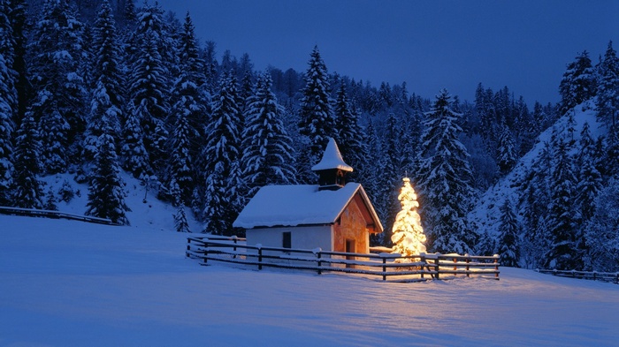 Snowy chapel with illuminated Christmas tree at dusk