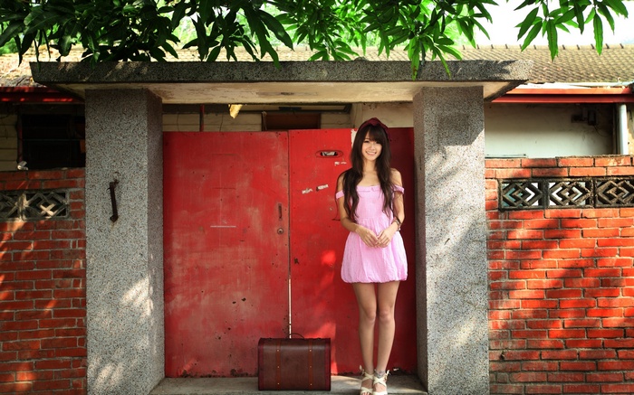 Woman in pink dress with suitcase in front of red doors