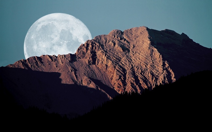 Full moon behind a rocky mountain peak