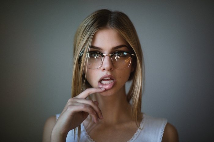 Woman with blonde hair wearing glasses and finger on lips