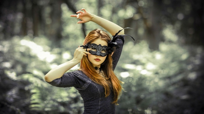 Woman wearing a black masquerade mask in a forest