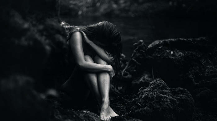 A woman sits alone in a dark, rocky environment
