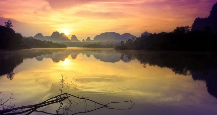 Thailand lake at sunrise with misty mountains and reflections