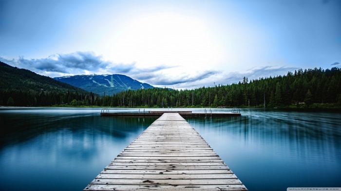 Wooden pier on a calm lake with mountains and forest