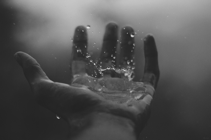 Monochrome image of water drops falling on an open hand