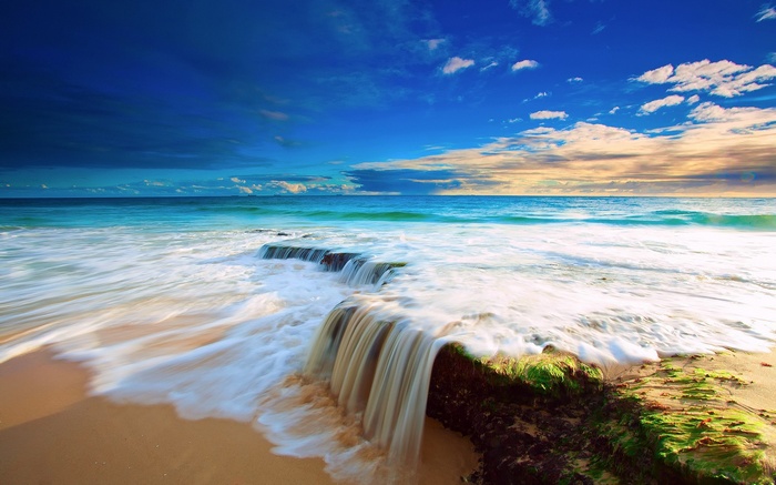 Ocean waves crashing on a sandy beach with rocks