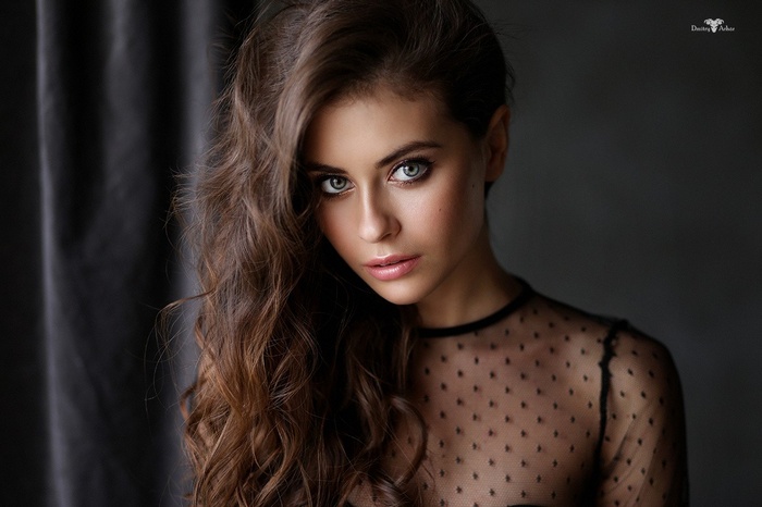 Woman with long wavy brunette hair wearing sheer black top