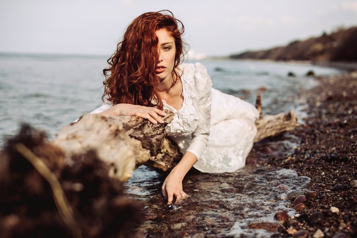 Redhead woman in white dress on a log by the water