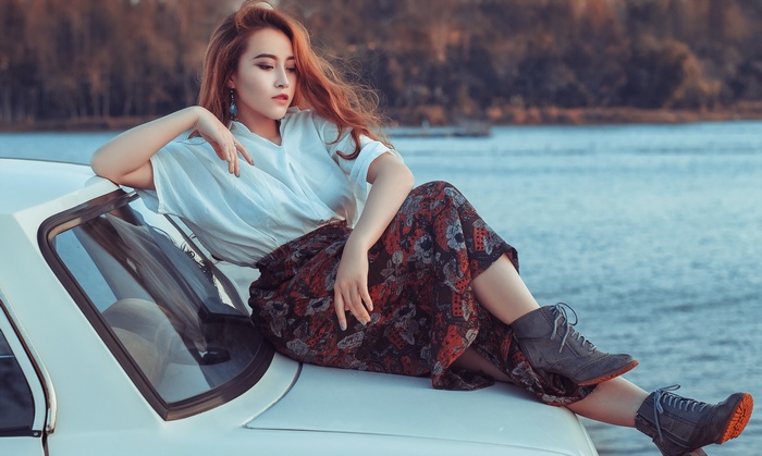 Asian woman sitting on a white car by the water